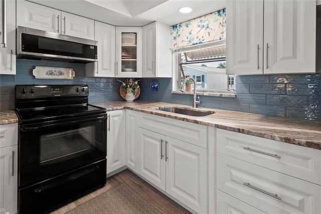 kitchen featuring stainless steel microwave, white cabinets, black range with electric stovetop, and a sink