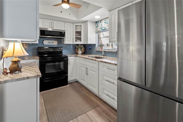 kitchen featuring a ceiling fan, light wood finished floors, a tray ceiling, a sink, and appliances with stainless steel finishes