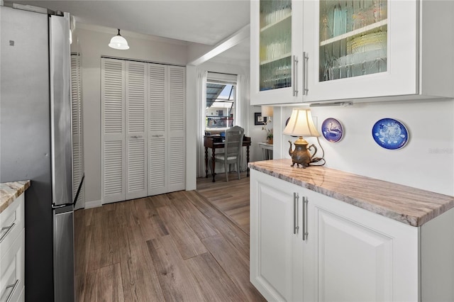 kitchen featuring glass insert cabinets, light stone counters, freestanding refrigerator, wood finished floors, and white cabinetry