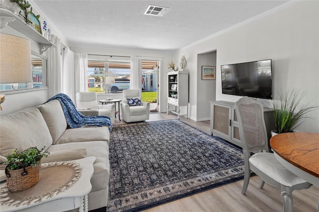 living area with ornamental molding, wood finished floors, visible vents, and a textured ceiling