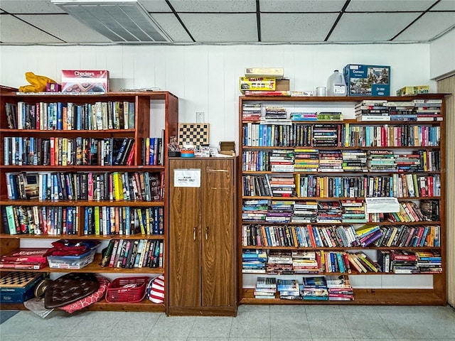 interior space featuring tile patterned floors, wall of books, and a paneled ceiling