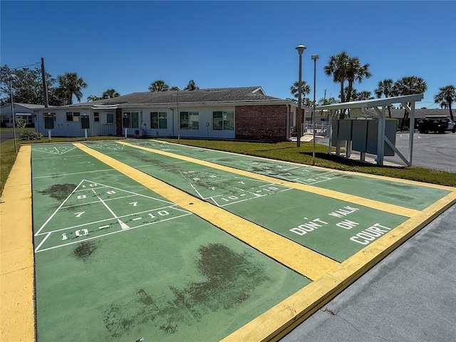 view of property's community with shuffleboard, uncovered parking, and a lawn