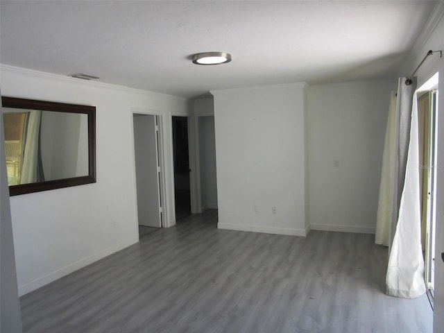 empty room with visible vents, baseboards, wood finished floors, and crown molding