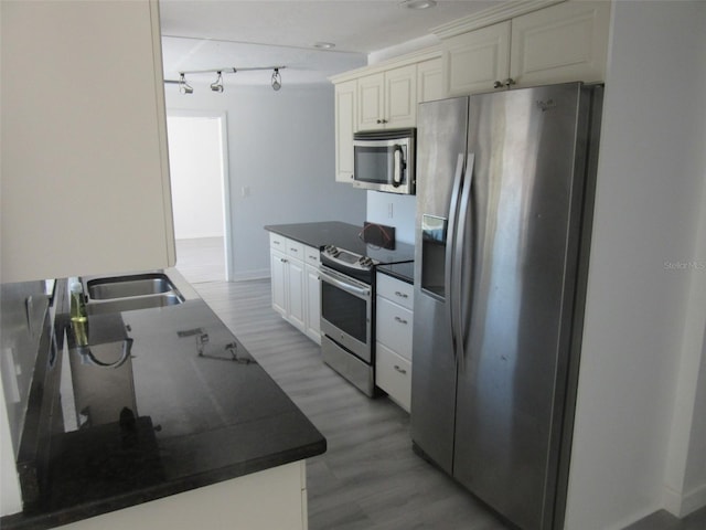 kitchen with dark countertops, appliances with stainless steel finishes, light wood-style floors, and a sink