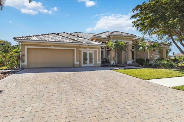 mediterranean / spanish-style home featuring an attached garage, stucco siding, french doors, a tile roof, and decorative driveway