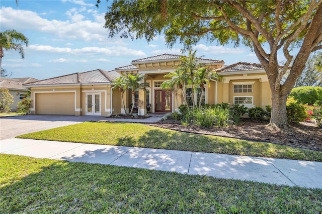 mediterranean / spanish-style house featuring stucco siding, french doors, an attached garage, and a front yard