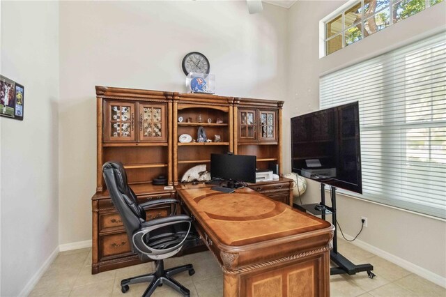 home office featuring light tile patterned floors, baseboards, and a towering ceiling