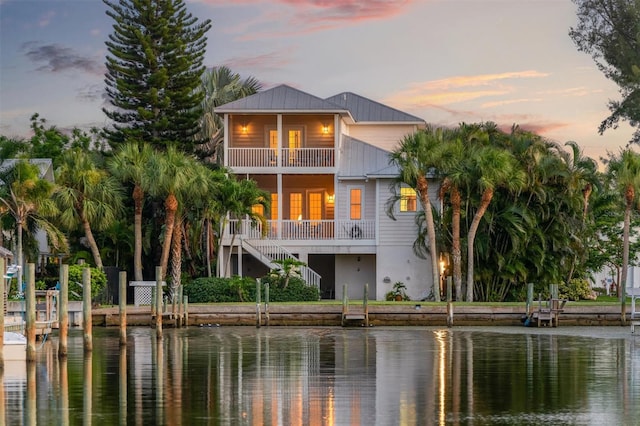 rear view of property with metal roof, a water view, a balcony, and stairs