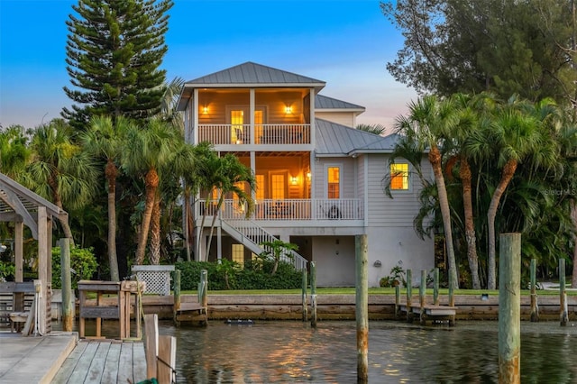 back of house at dusk featuring metal roof, a water view, stairway, and a standing seam roof