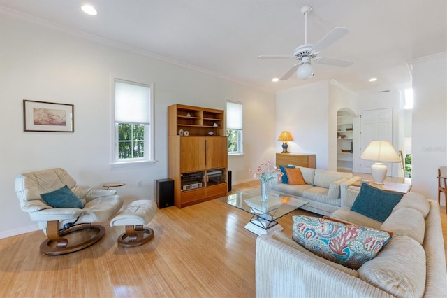 living area featuring arched walkways, baseboards, light wood-style floors, and ornamental molding