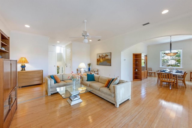 living area with visible vents, ornamental molding, recessed lighting, arched walkways, and light wood-style floors