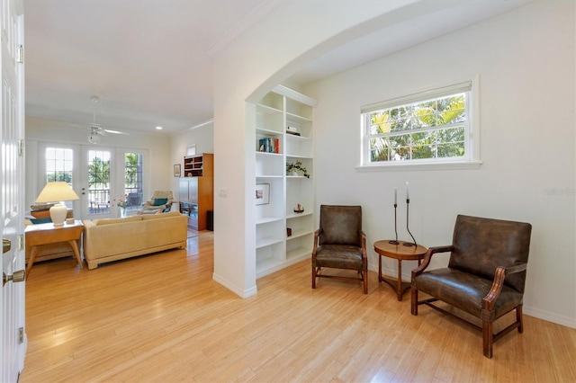 living area with baseboards, built in features, ornamental molding, light wood-style flooring, and french doors