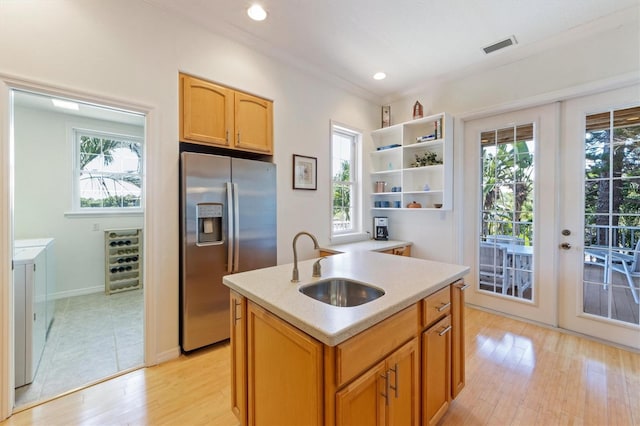 kitchen featuring washer and clothes dryer, light wood-type flooring, light countertops, stainless steel refrigerator with ice dispenser, and a kitchen island with sink