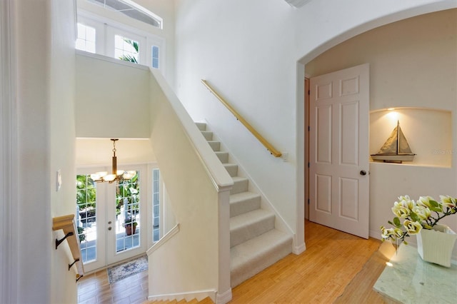 stairway featuring a high ceiling, wood finished floors, arched walkways, and french doors