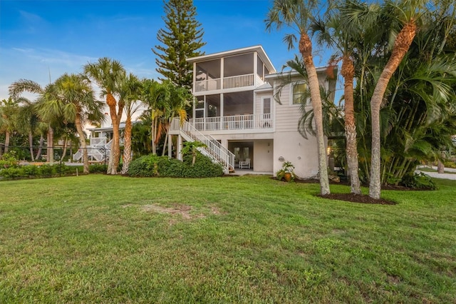 rear view of house with stairs, a yard, and a sunroom