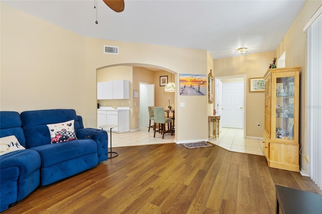 living area with visible vents, baseboards, ceiling fan, light wood-type flooring, and arched walkways