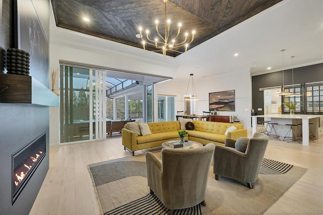 living room featuring light wood-style flooring, a raised ceiling, a notable chandelier, and ornamental molding