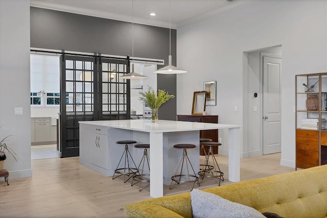 kitchen with light wood finished floors, a kitchen island, a breakfast bar, light countertops, and crown molding