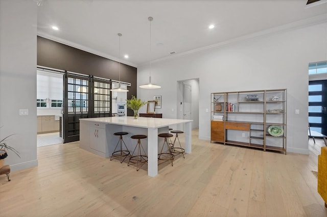 kitchen featuring baseboards, a large island, ornamental molding, and light wood finished floors