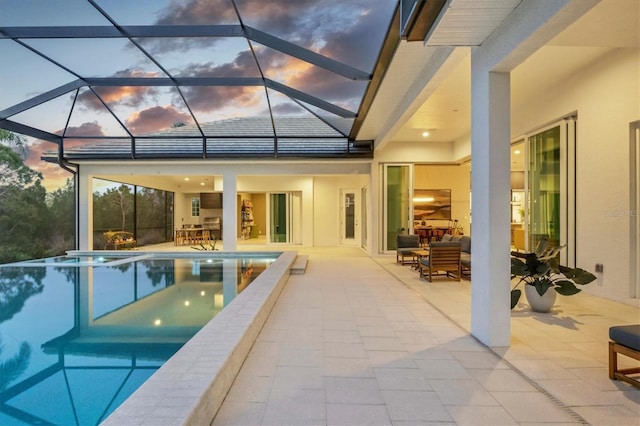 pool at dusk with glass enclosure, a patio area, an infinity pool, and outdoor dining space