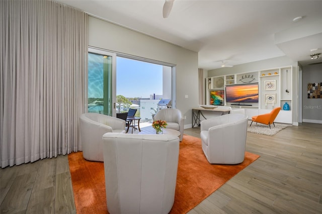 living area featuring light wood finished floors, built in shelves, a ceiling fan, and baseboards