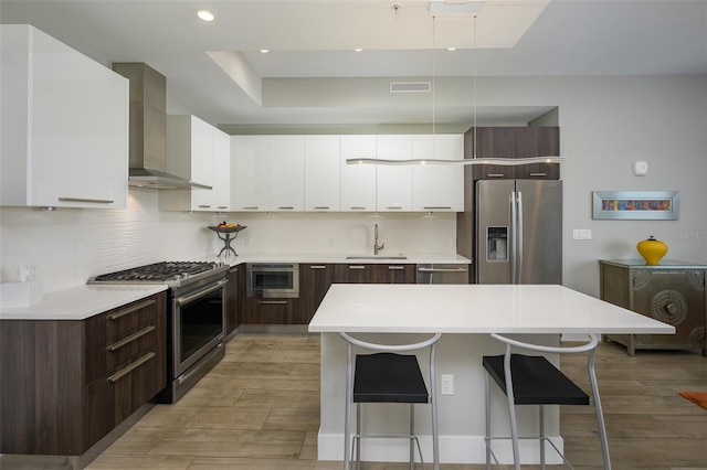 kitchen with a breakfast bar, a sink, stainless steel appliances, wall chimney range hood, and modern cabinets