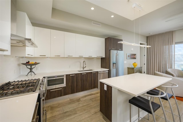 kitchen with dark brown cabinets, a breakfast bar area, appliances with stainless steel finishes, white cabinetry, and a sink