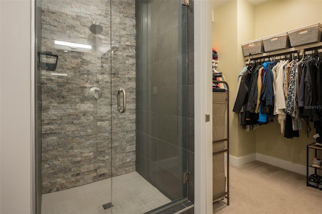 bathroom featuring a walk in closet, a shower stall, and baseboards