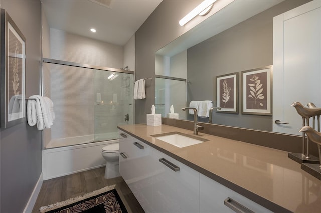 bathroom featuring toilet, recessed lighting, wood finished floors, combined bath / shower with glass door, and vanity