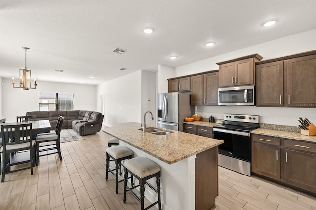 kitchen with wood finish floors, visible vents, a breakfast bar, a sink, and stainless steel appliances