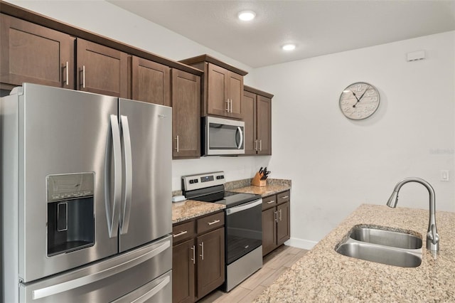 kitchen with light stone counters, wood finish floors, a sink, stainless steel appliances, and dark brown cabinets