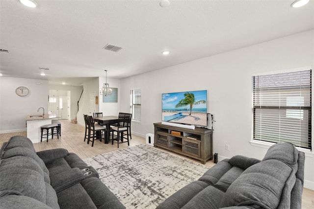 living area with visible vents, baseboards, light wood-type flooring, and an inviting chandelier