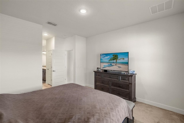 bedroom featuring visible vents, baseboards, light colored carpet, and ensuite bath