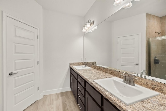 full bathroom featuring double vanity, a stall shower, baseboards, and a sink