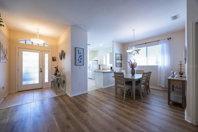 foyer with visible vents, a textured ceiling, wood finished floors, an inviting chandelier, and baseboards