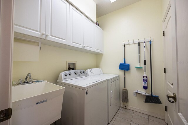 clothes washing area with cabinet space, light tile patterned floors, washer and dryer, and a sink