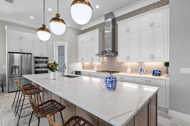 kitchen featuring a sink, a spacious island, stainless steel appliances, crown molding, and wall chimney range hood