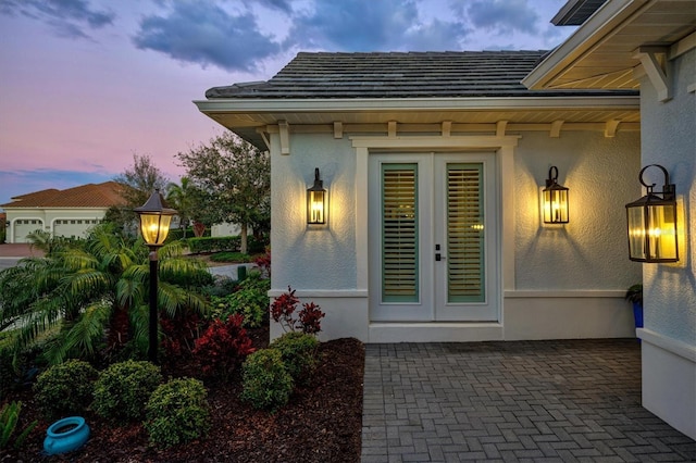 exterior entry at dusk with stucco siding and french doors