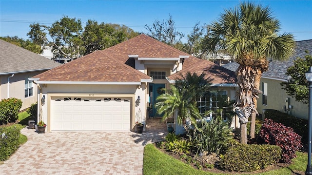 view of front of home featuring a garage, stucco siding, decorative driveway, and roof with shingles