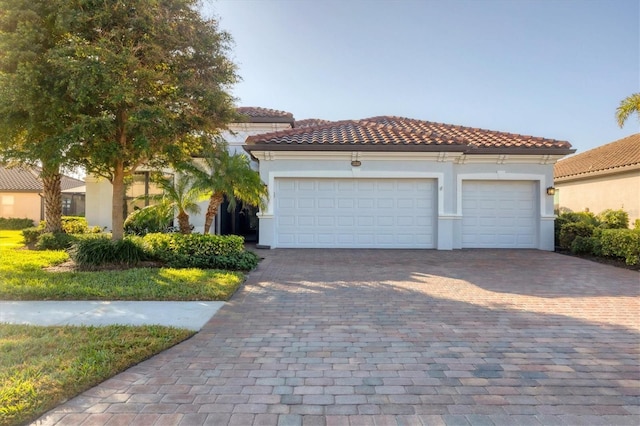 mediterranean / spanish home with a tiled roof, decorative driveway, an attached garage, and stucco siding