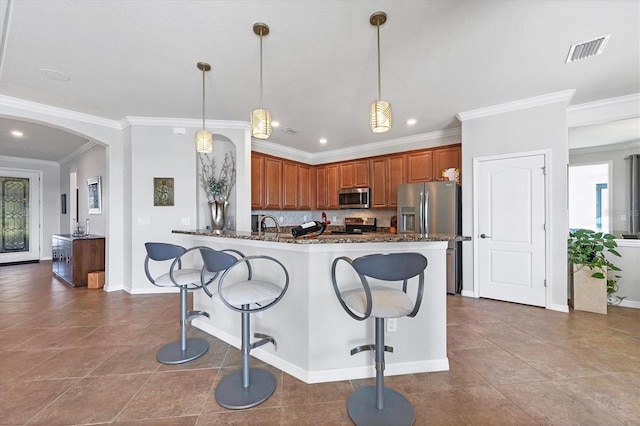 kitchen with a breakfast bar area, brown cabinetry, visible vents, arched walkways, and stainless steel appliances