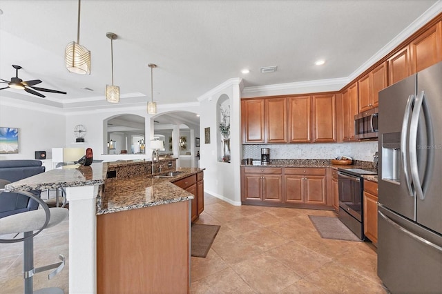 kitchen featuring a breakfast bar area, dark stone counters, a sink, stainless steel appliances, and crown molding