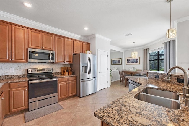 kitchen with pendant lighting, ornamental molding, appliances with stainless steel finishes, brown cabinetry, and a sink