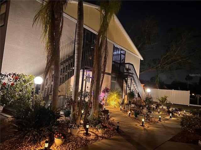 property exterior at night featuring stairs, fence, and stucco siding