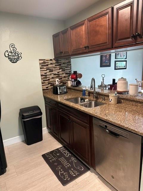 kitchen with dark brown cabinets, backsplash, dishwasher, dark stone counters, and a sink