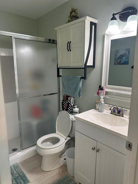 bathroom featuring toilet, a stall shower, vanity, and wood finished floors