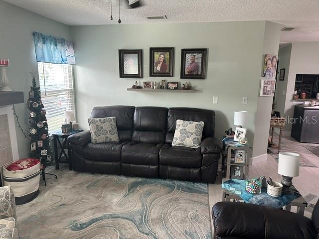 living room with ceiling fan, visible vents, and a textured ceiling