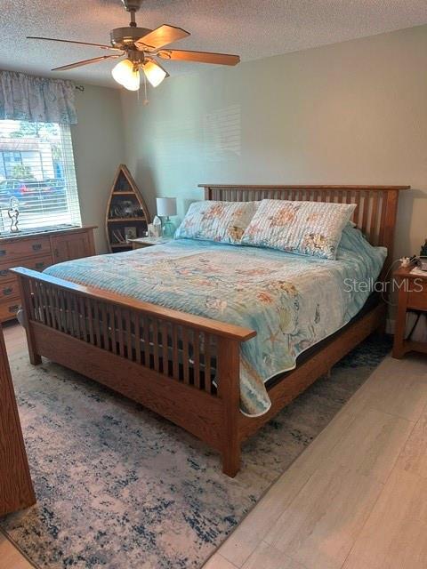 bedroom featuring ceiling fan, wood finished floors, and a textured ceiling