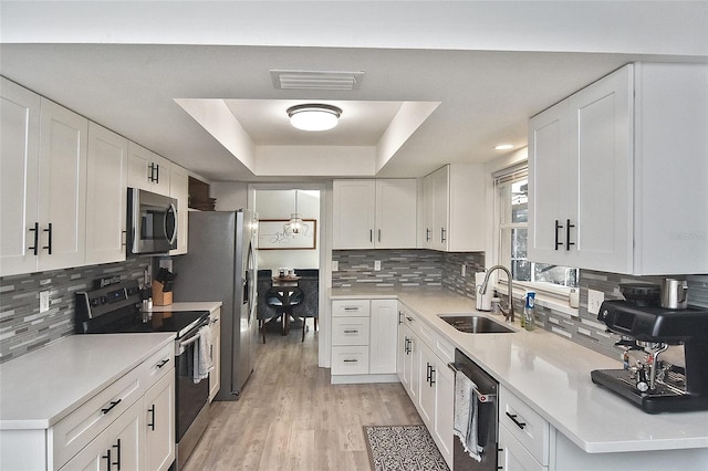 kitchen featuring visible vents, a sink, white cabinetry, stainless steel appliances, and a raised ceiling