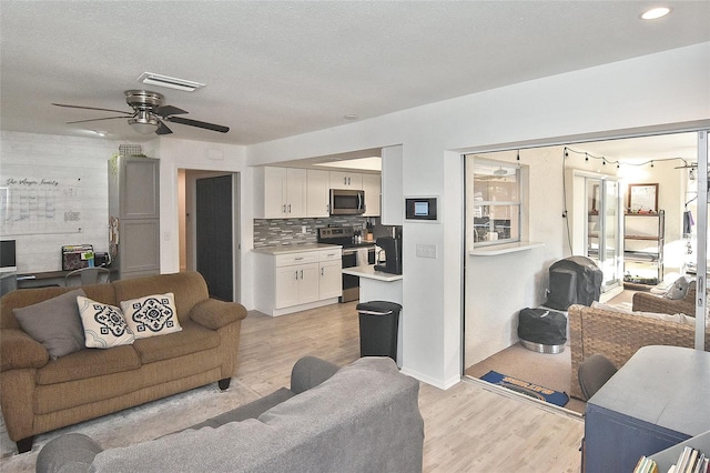 living area featuring ceiling fan, visible vents, a textured ceiling, and light wood-style flooring